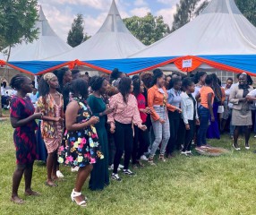 line of women smiling and standing in front of white tent with orange and blue bunting